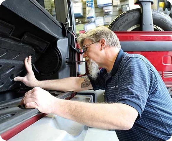 Technician installing a speaker into a red golf cart body panel in the service shop
